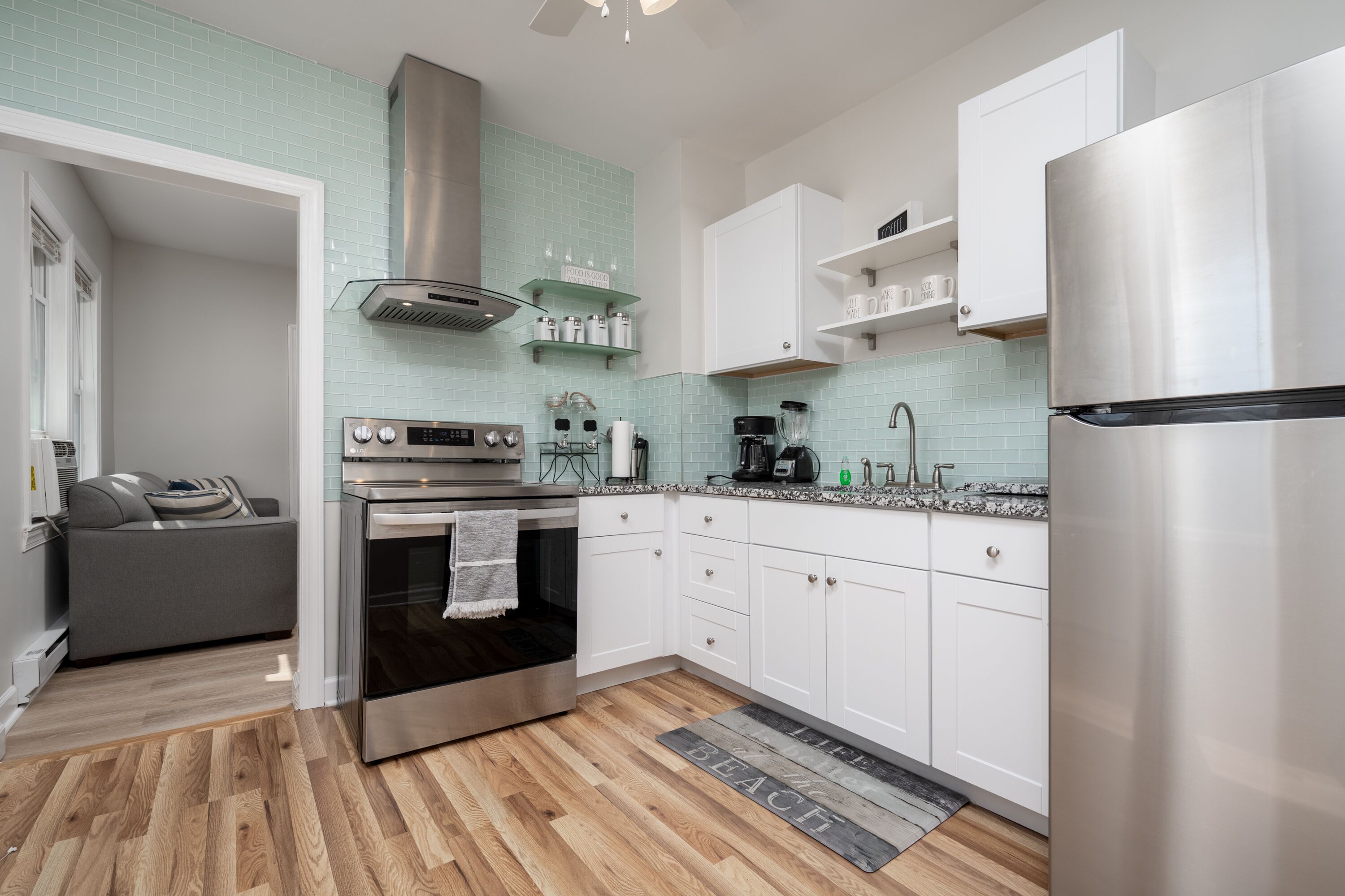 A modern kitchen with stainless steel appliances, white cabinetry, and a wooden floor.