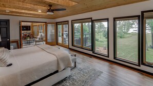 Une chambre avec un grand lit, un ventilateur de plafond et une vue sur une terrasse et un jardin.