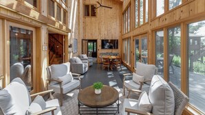 Un intérieur spacieux en bois, avec de hauts plafonds, de grandes fenêtres et un espace salon central agrémenté de canapés et d’une table basse.
