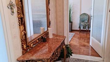 Un couloir avec une console en marbre, un grand miroir décoratif et une plante en pot.