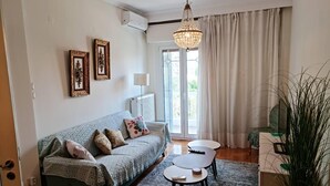 A living room with a sofa, two small tables, a chandelier, and a large plant. - Fairytale, Nilie Hospitality MGMT (Thessaloniki)