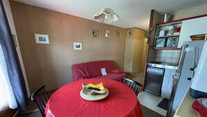 A compact kitchen with a dining table, chairs, and a red tablecloth. - Griou N°52 (Le Lioran)