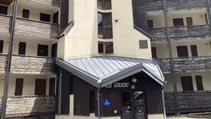 A multi-story building with a central vertical structure, balconies, and a ground-level entrance labeled "LE GRIOU". - Griou N°52 (Le Lioran)
