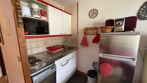 A compact kitchen with white cabinets, a stainless steel refrigerator, and a dishwasher. - Griou N°52 (Le Lioran)