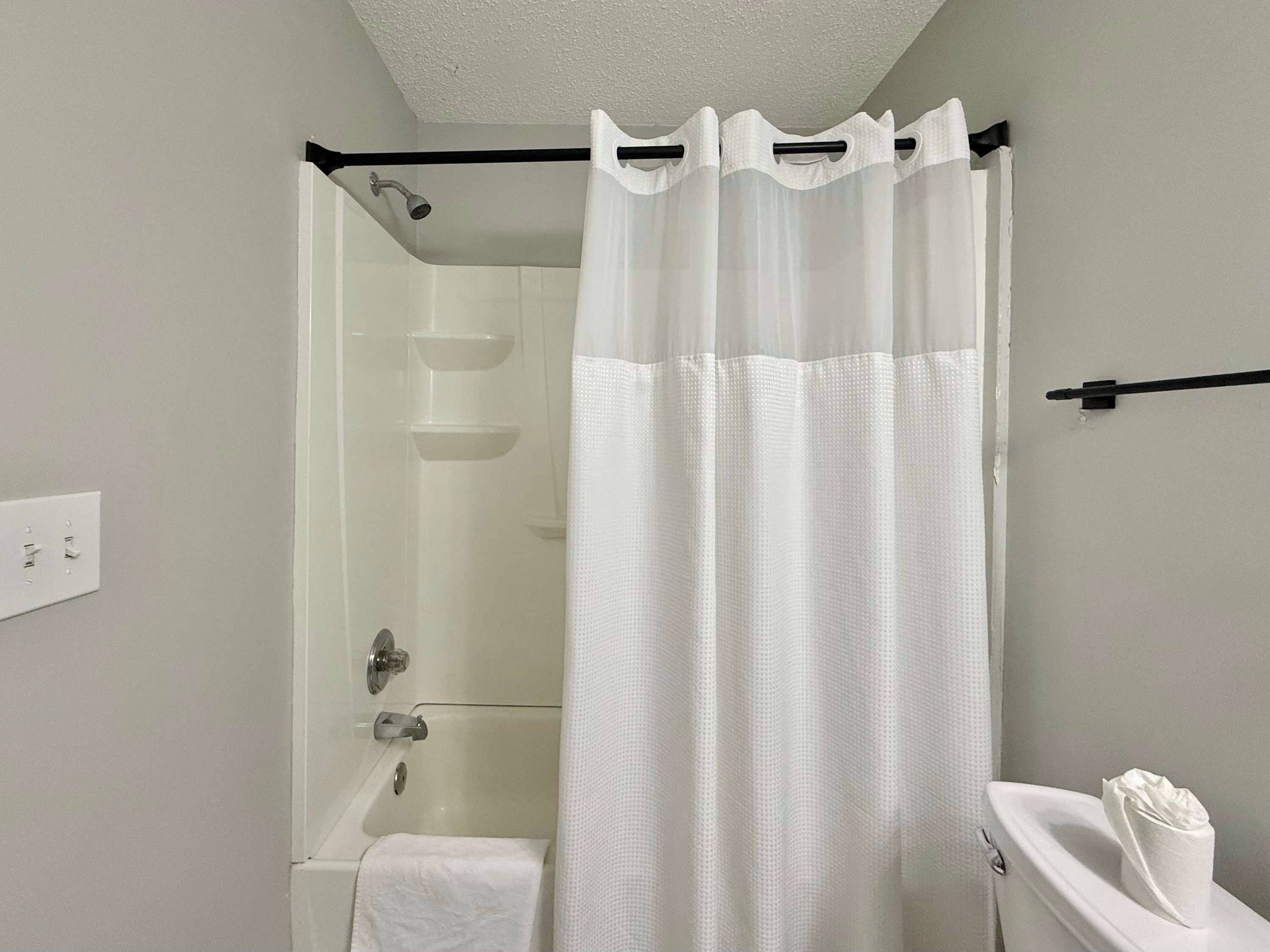 A bathroom with a shower, toilet, and a white curtain.