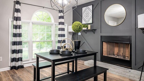 A modern living room with a fireplace, a dining table with chairs, a large window with curtains, and a geometric light fixture. - Renovated townhouse in Norcross (Norcross)