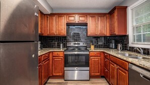 A kitchen with wooden cabinets, a stainless steel refrigerator, a stove, and a dishwasher. - Renovated townhouse in Norcross (Norcross)