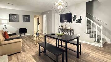 A modern living room with a dining table, sofa, and a staircase.