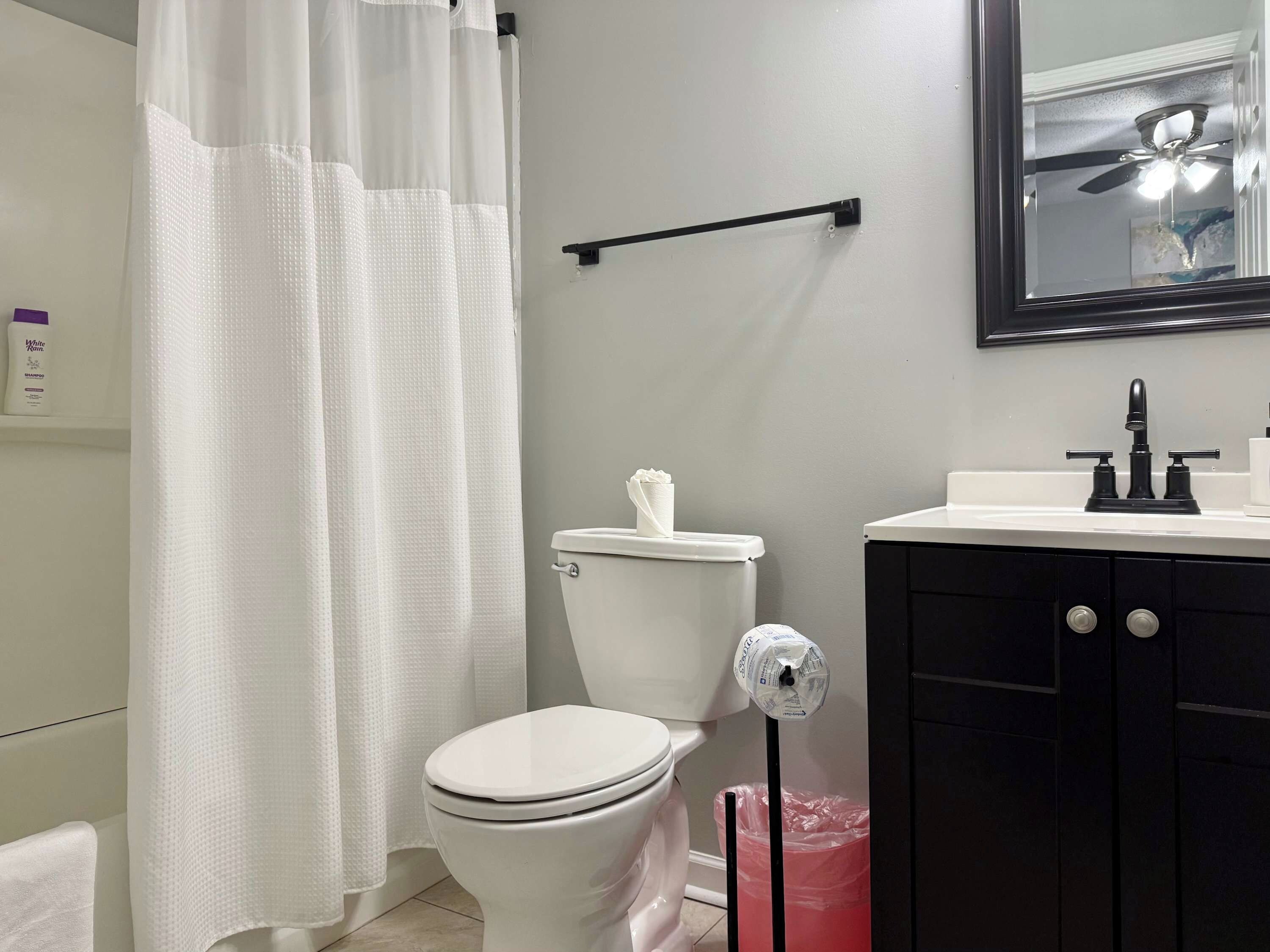 Un baño con inodoro, lavamanos blanco, espejo y cortina de ducha.