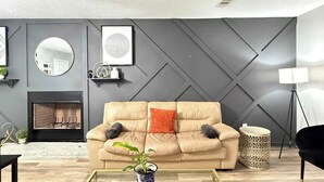 Un salon moderne avec un canapé beige, une table basse en verre, une cheminée et un panneau décoratif mural.