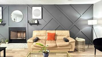 A modern living room with a beige sofa, a glass coffee table, a fireplace, and a decorative wall panel.