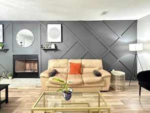 Una sala de estar moderna con un sofá color crema, una mesa de centro de vidrio, una chimenea y un panel decorativo en la pared.