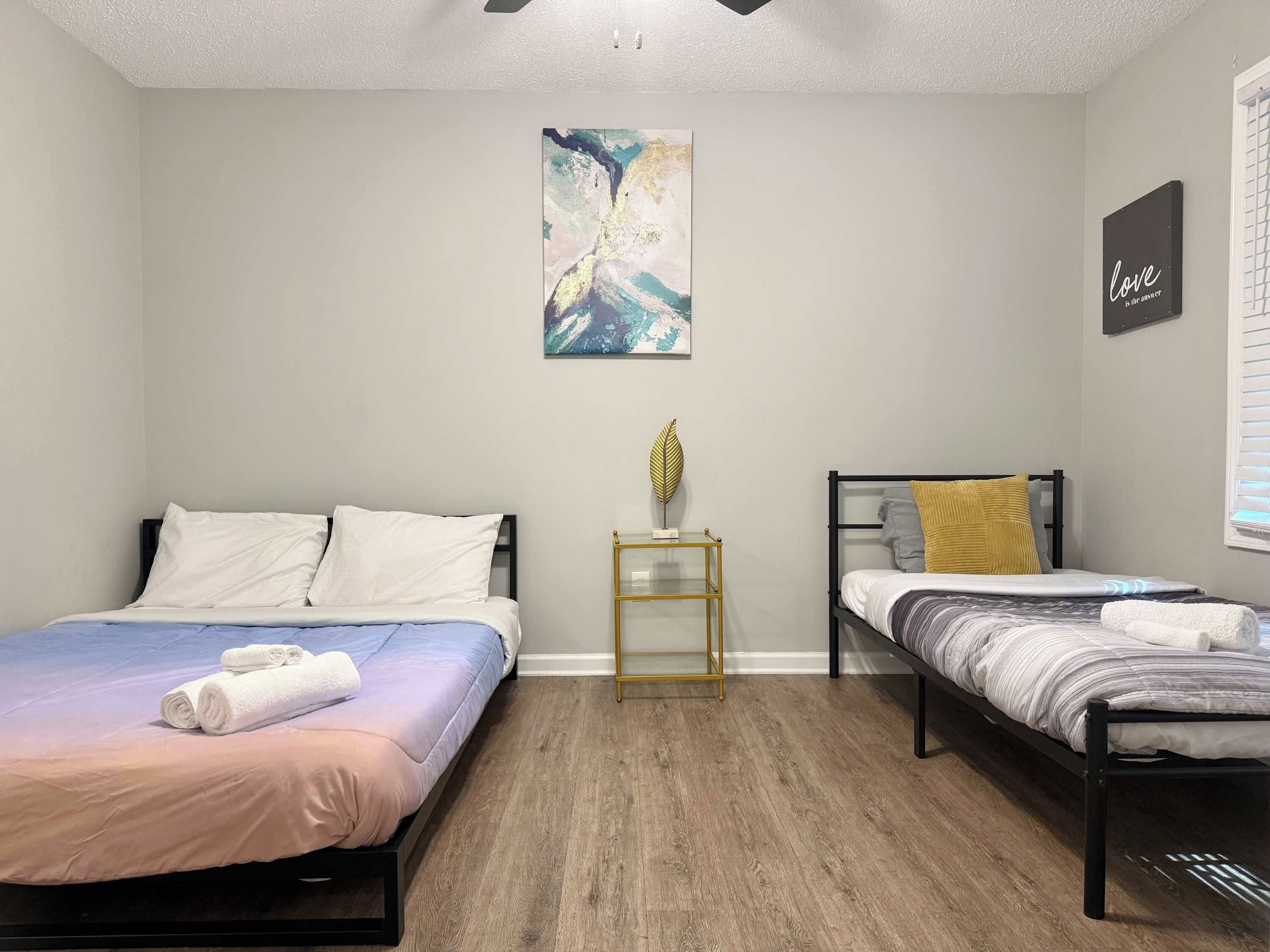 A bedroom with two beds, a small table, a wall art piece, and a sign.