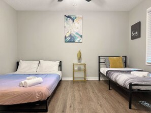 A bedroom with two beds, a small table, a wall art piece, and a sign.