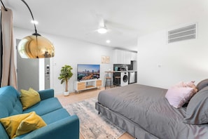 Een modern appartement met een bank, een bed, een televisie, een keuken en een plafondventilator.