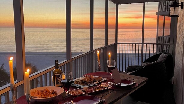 A balcony table set with dinnerware, candles, and wine glasses, overlooking a sunset over the ocean. - New to Rental market Luxury remodeled condo located directly on Siesta Key Beach (Sarasota)