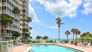A swimming pool with lounge chairs and palm trees, surrounded by a high-rise building. - New to Rental market Luxury remodeled condo located directly on Siesta Key Beach (Sarasota)