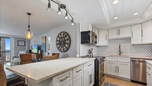 A modern kitchen with white cabinets, a large island, stainless steel appliances, and a dining area with wicker chairs. - New to Rental market Luxury remodeled condo located directly on Siesta Key Beach (Sarasota)