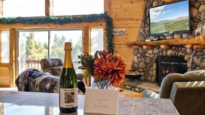 A wooden cabin interior with a stone fireplace, a television mounted on the wall, a bottle of champagne, and a welcome sign.