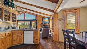 A rustic kitchen with wooden cabinets, a dishwasher, and a large window overlooking a scenic view.