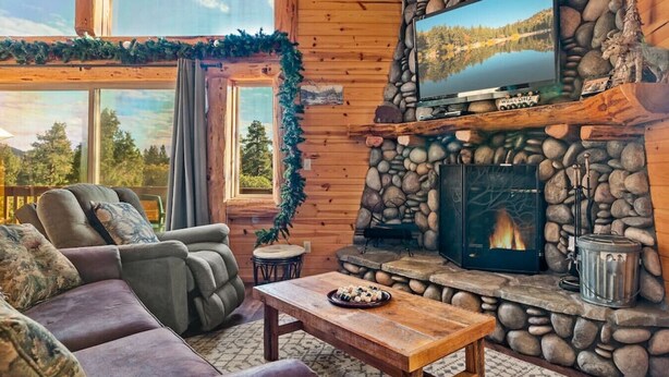 A cozy cabin interior with a stone fireplace, a comfortable seating area, and a television mounted above it.
