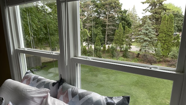 Una camera da letto con un'ampia finestra, un letto con cuscini decorati e vista su un prato verde e alberi.