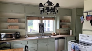 Una cucina con microonde, macchina del caffè, lavello e fornello. Si vede una finestra con vista sull'esterno e un cartello applicato al vetro.