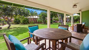 Une terrasse couverte avec une table ronde en bois et des chaises, entourée d’un jardin luxuriant et offrant une vue sur un quartier résidentiel.