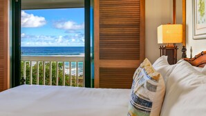 Ein Hotelzimmer mit Bett, Nachttisch mit Lampe und Blick auf das Meer durch eine offene Tür.