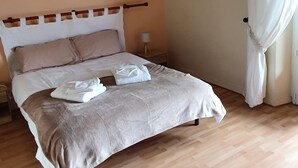 A neatly made bed with a wooden headboard, a bedside table with a lamp, and a large window with white curtains. - Large 3* house in Périgord 10 minutes from Sarlat (Marquay)