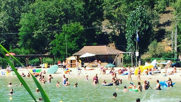 A beach with people swimming and sunbathing, a small hut, and greenery in the foreground. - Large 3* house in Périgord 10 minutes from Sarlat (Marquay)