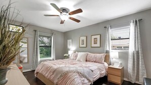 Ein Schlafzimmer mit Bett, Nachttischen, Deckenventilator und einem Fenster mit Vorhängen.