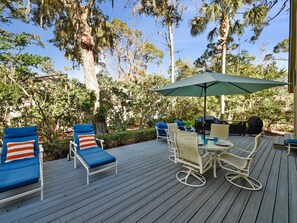 Une terrasse extérieure avec des chaises longues et une table, entourée d’arbres et de verdure.