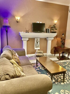 Una sala de estar con chimenea, un sofá, una mesa de centro y una televisión.