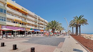 Ein Hotel direkt am Strand mit Außenbestuhlung, Palmen und blauem Himmel.