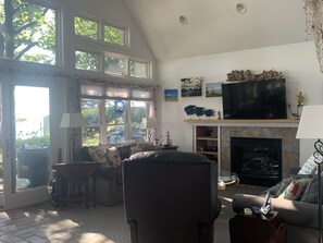 Un salon spacieux doté d’une cheminée, d’un grand téléviseur et offrant une vue sur l’extérieur grâce à de grandes fenêtres.