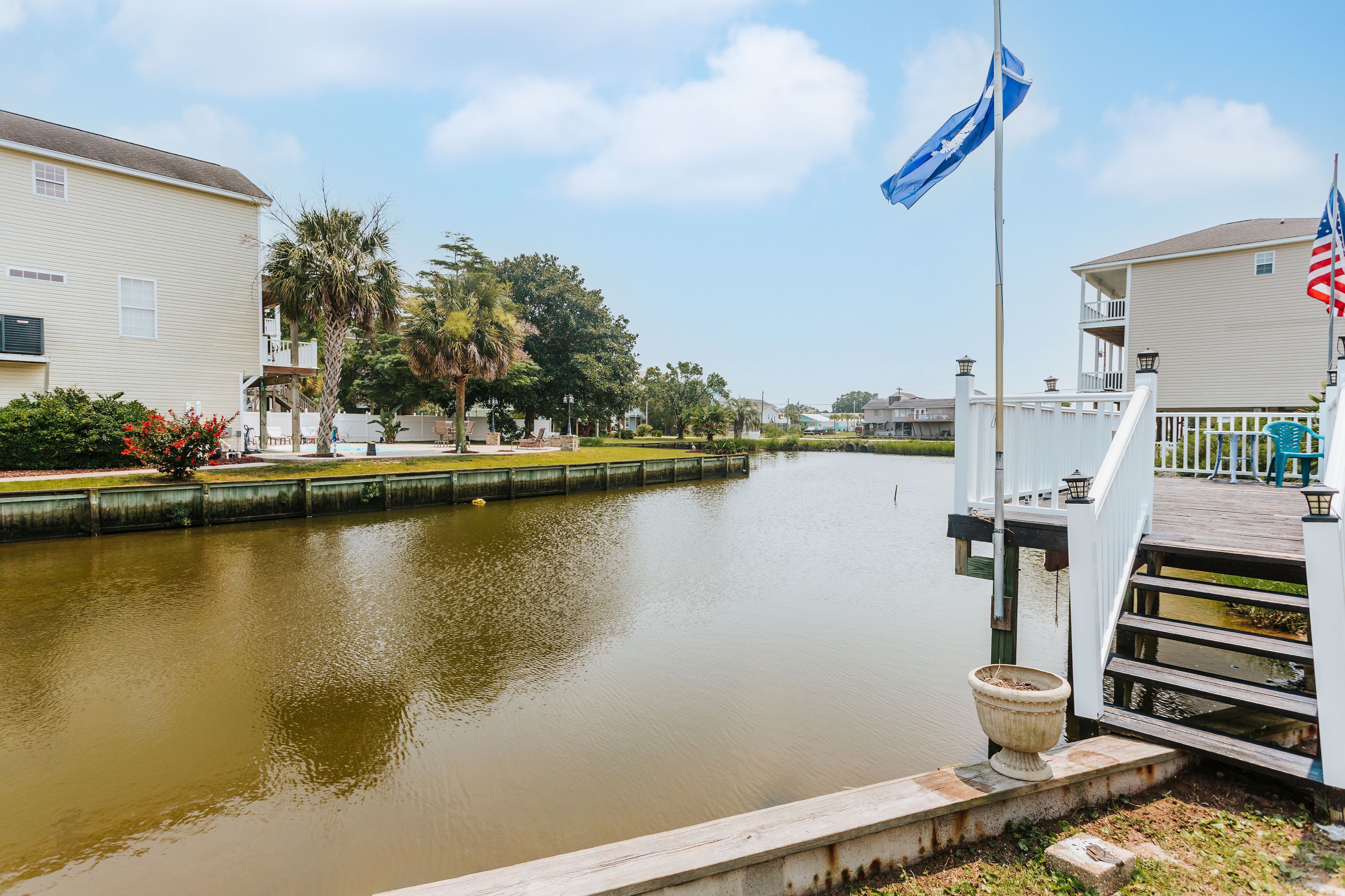 A canal with a wooden dock and a flagpole with flags.