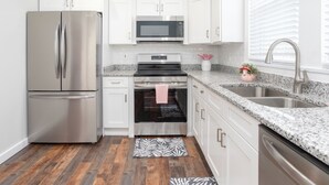 Una cocina con armarios blancos, electrodomésticos de acero inoxidable, encimeras de granito y piso de madera.