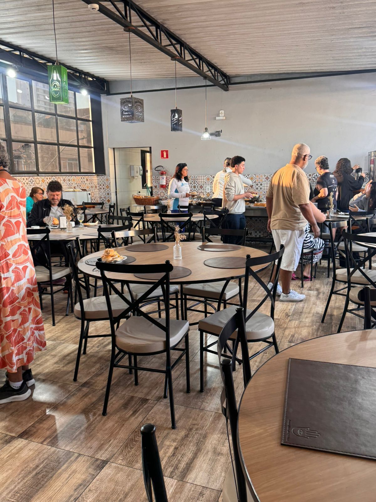 A restaurant with round tables and chairs, a counter with staff, and a tiled backsplash.