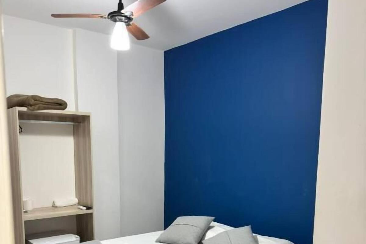 Un dormitorio con cama, ventilador de techo y una pared azul decorativa.