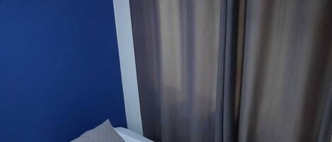A single bed with a grey blanket and pillow, a white mattress, and a grey quilted cover.