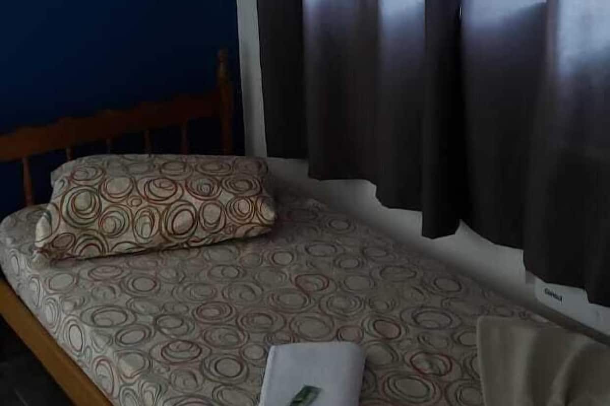 Una cama individual con una colcha estampada, una almohada y un ordenador portátil encima.