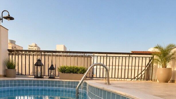 Una piscina en la azotea con borde de baldosas, barandilla metálica y plantas en macetas.