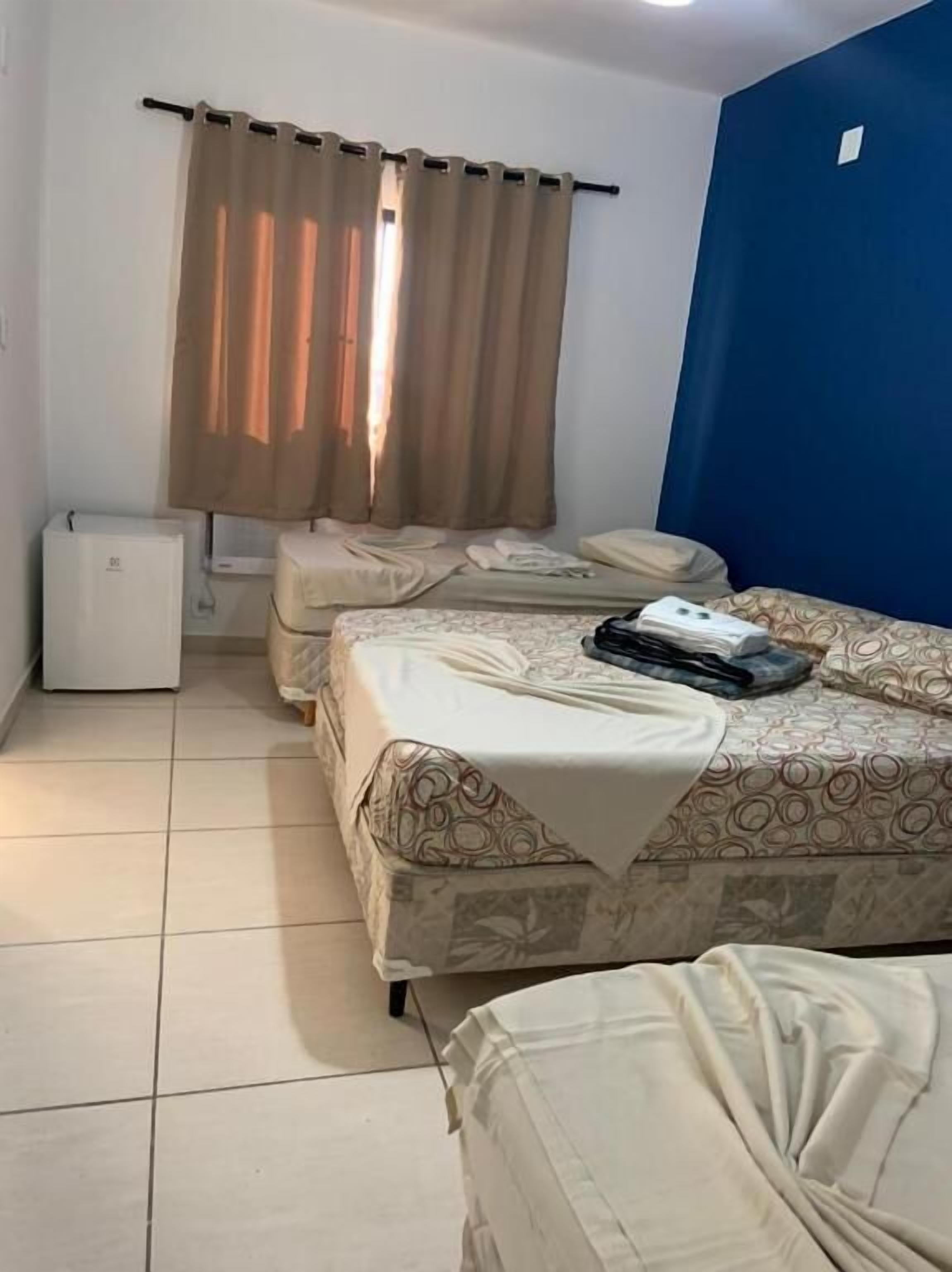 A small, clean room with two beds, a heater, and a window with curtains.
