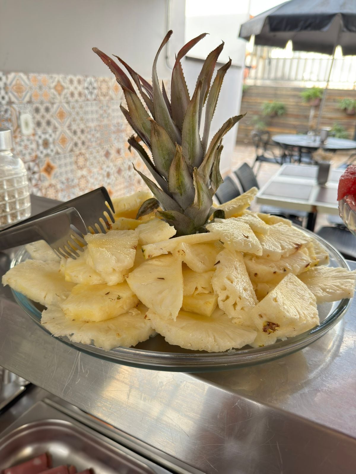 Un cuenco de vidrio con trozos de piña sobre una mesa de acero inoxidable.