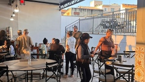 Un área de comedor al aire libre con mesas y sillas redondas, techo metálico y vistas a edificios al fondo.
