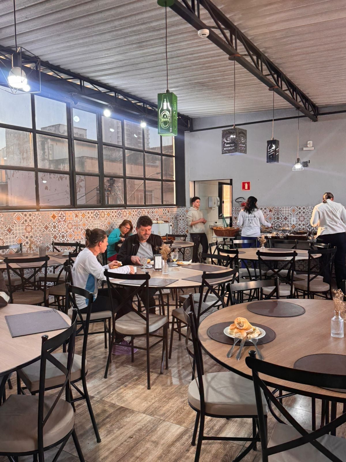A restaurant with multiple tables and chairs, a tiled backsplash, and hanging pendant lights.