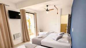 Una habitación de hotel con dos camas, un ventilador de techo, un televisor y una puerta corrediza a un balcón.