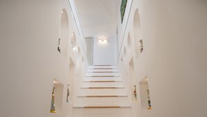 Una escalera con paredes blancas y peldaños de madera que conducen a una lámpara en el techo.