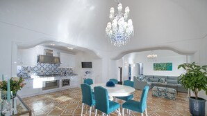 Un salón amplio con una mesa redonda y sillas azules, un sofá gris y una planta grande en maceta.